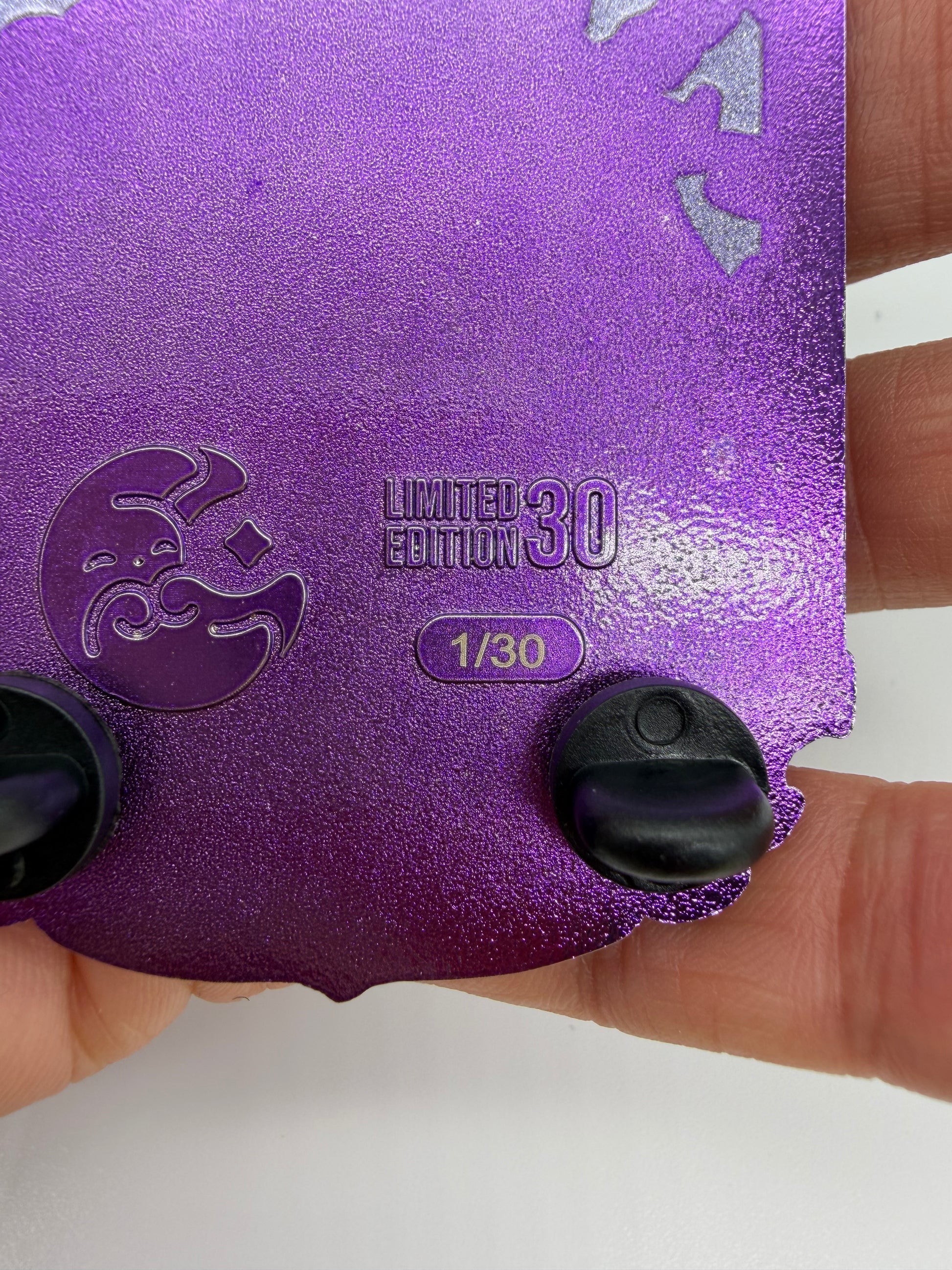 A close-up of a purple glittery collectible card or sticker being held by a hand. The card features a crescent moon emblem, the text 'LIMITED EDITION 30' and '1/30', and two black plastic tabs on the bottom edge.