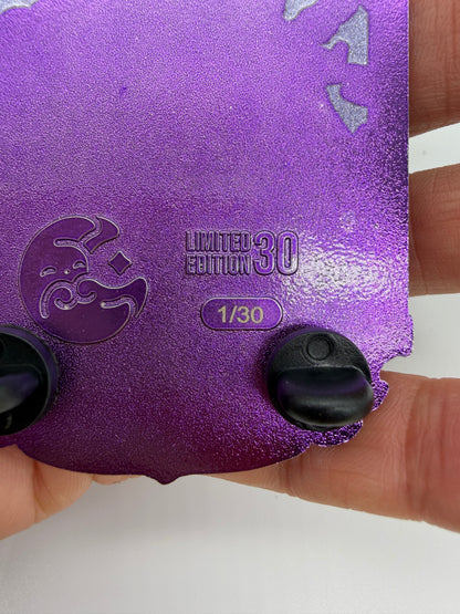 A close-up of a purple glittery collectible card or sticker being held by a hand. The card features a crescent moon emblem, the text 'LIMITED EDITION 30' and '1/30', and two black plastic tabs on the bottom edge.